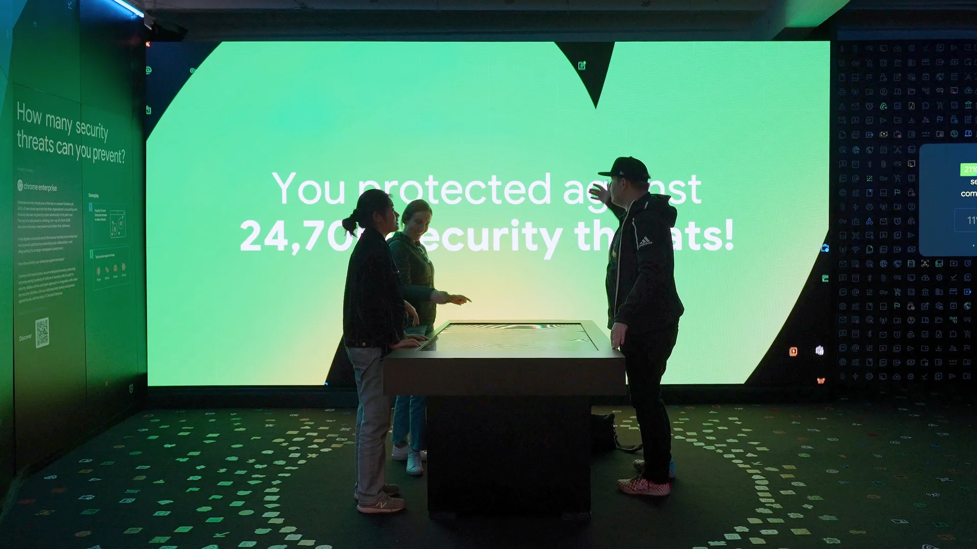 Three people standing around the touchscreen table after a successful game of Data Defense. The big LED screen behind them shows their achieved high score.